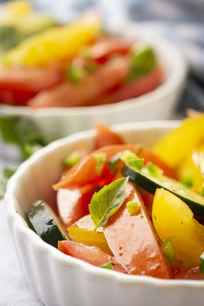 A closeup picture of a serving of Spicy Tomato Cucumber Salad showing bits of jalapeno and a tiny basil leave garnishing the edge.