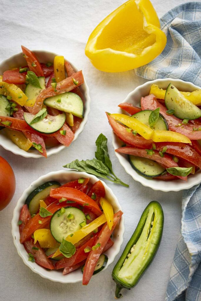 Looking down onto three small white ramekins with fluted edges containing a colorful mixure of tomato, cucumber and yellow bell pepper. Spicy Tomato Cucumber Salad